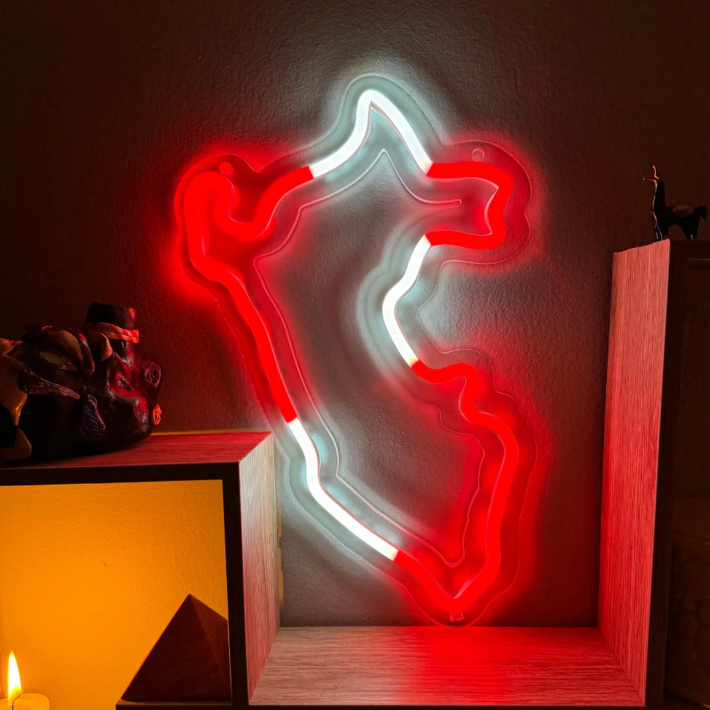 LED Neon sign shaped like the map of Peru, illuminated with vibrant red and white lights, mounted on a wall with decorative items surrounding it, creating a warm and nostalgic atmosphere.